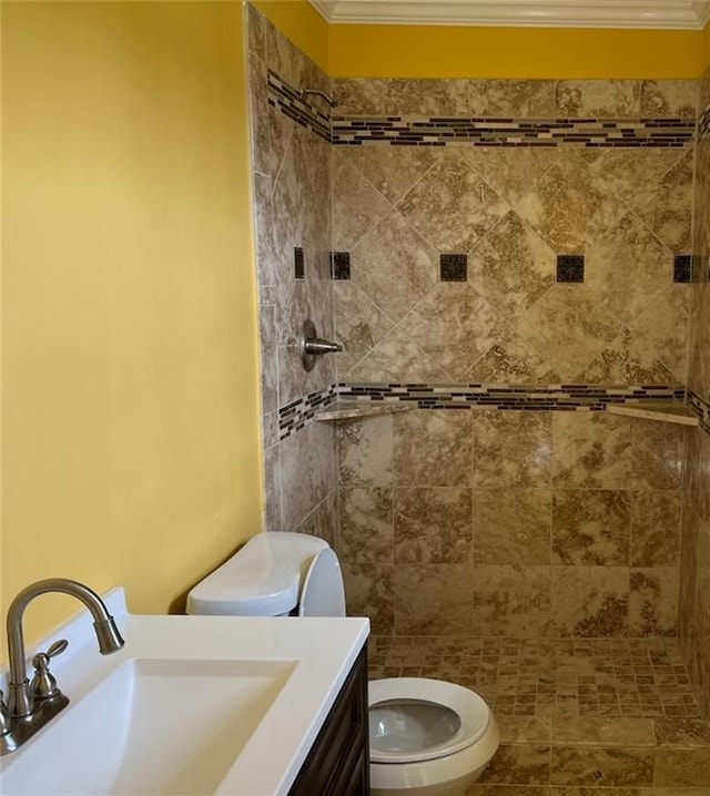 bathroom featuring ornamental molding, a tile shower, vanity, and toilet