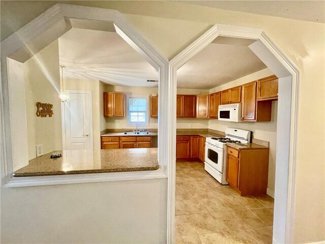 kitchen featuring light tile patterned floors, sink, kitchen peninsula, white appliances, and light stone countertops