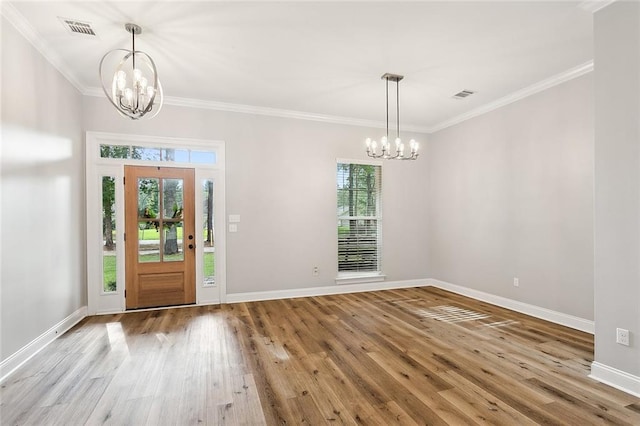 foyer entrance with light wood-type flooring, ornamental molding, and a notable chandelier