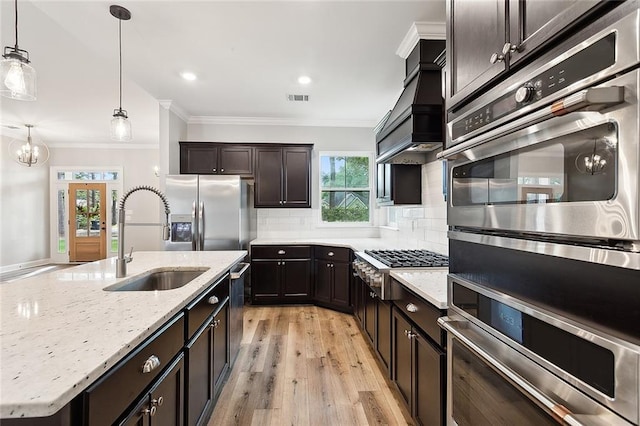 kitchen featuring light hardwood / wood-style floors, tasteful backsplash, sink, hanging light fixtures, and premium range hood