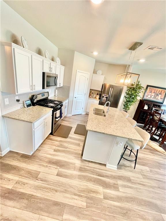 kitchen with stainless steel appliances, a kitchen island with sink, sink, pendant lighting, and white cabinetry