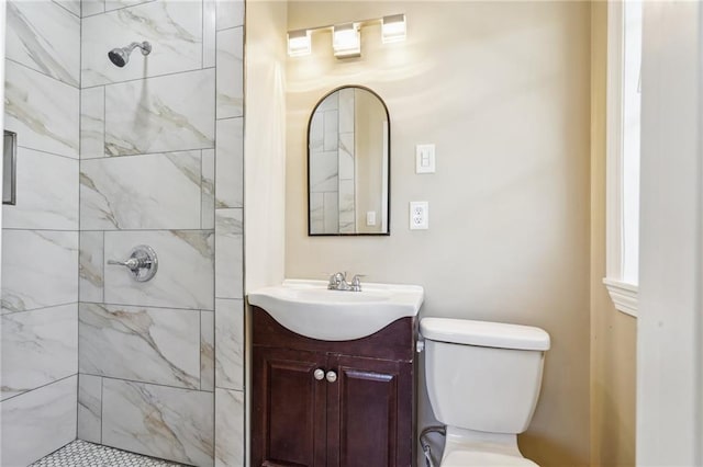 bathroom featuring a tile shower, vanity, and toilet