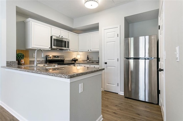 kitchen with sink, stainless steel appliances, dark hardwood / wood-style flooring, kitchen peninsula, and white cabinets