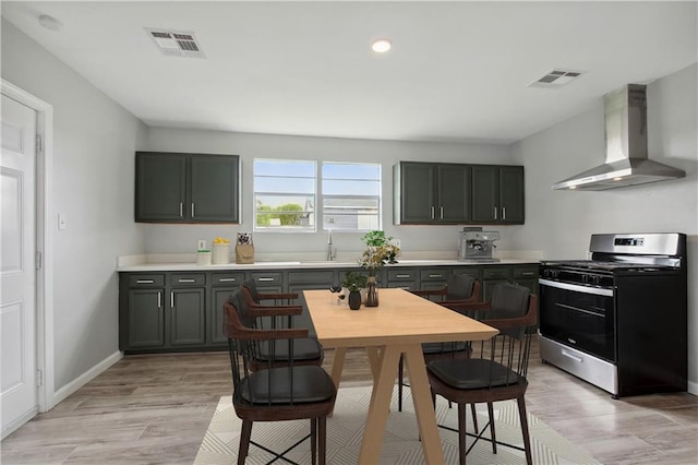 kitchen featuring gas range, sink, wall chimney range hood, and light wood-type flooring