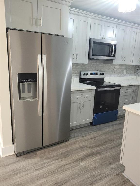 kitchen featuring stainless steel appliances, white cabinets, light wood-type flooring, and tasteful backsplash