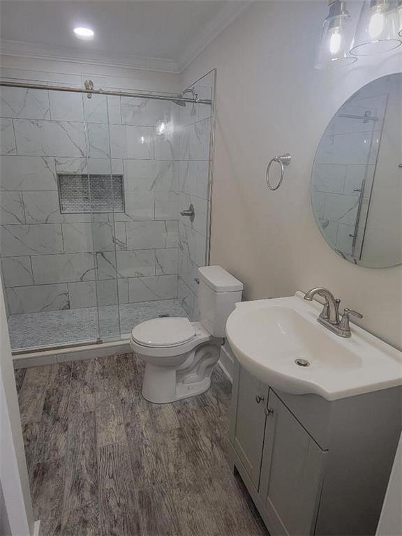 4985 Feliciana Dr, New Orleans, LA 70126 - bathroom featuring vanity, a shower stall, wood finished floors, ornamental molding, and toilet