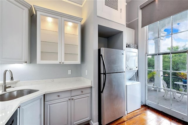 kitchen with white cabinetry, stainless steel refrigerator, stacked washer and clothes dryer, light stone countertops, and light hardwood / wood-style flooring