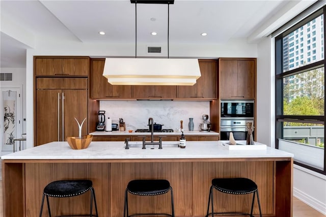 kitchen with a kitchen bar, built in appliances, hanging light fixtures, and a healthy amount of sunlight