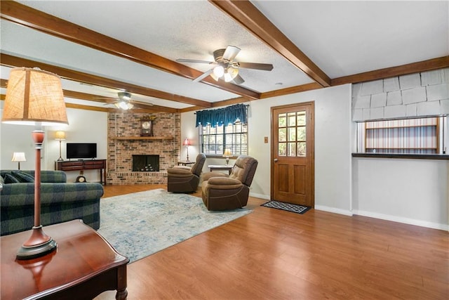 living room featuring ceiling fan, beamed ceiling, hardwood / wood-style flooring, and a fireplace