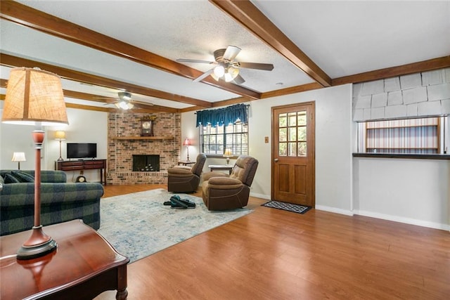 living room with wood-type flooring, a fireplace, beam ceiling, and ceiling fan