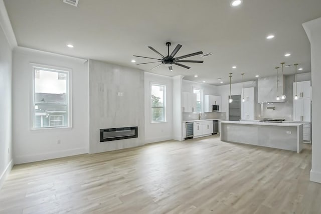 unfurnished living room featuring ceiling fan, sink, beverage cooler, light hardwood / wood-style flooring, and a fireplace