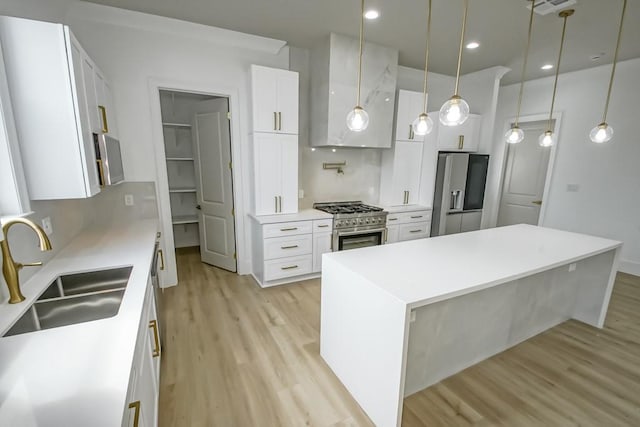 kitchen with sink, white cabinetry, hanging light fixtures, light hardwood / wood-style flooring, and stainless steel appliances