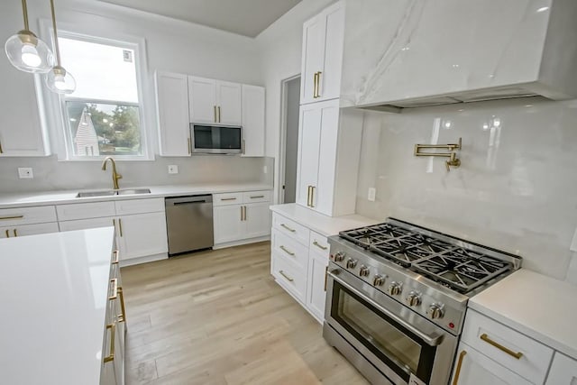 kitchen with appliances with stainless steel finishes, white cabinetry, range hood, light hardwood / wood-style flooring, and sink