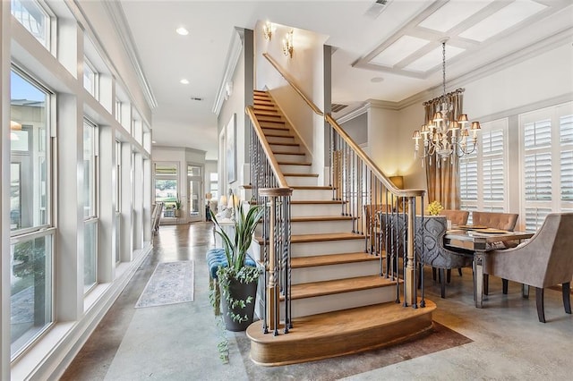 stairway featuring an inviting chandelier, a wealth of natural light, concrete floors, and ornamental molding