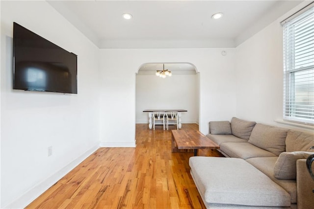 living room with baseboards, light wood-type flooring, arched walkways, and a wealth of natural light