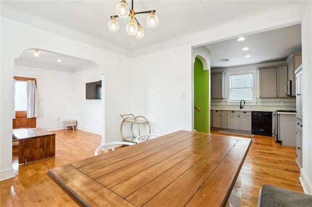 dining area with recessed lighting, arched walkways, an inviting chandelier, and light wood-style flooring