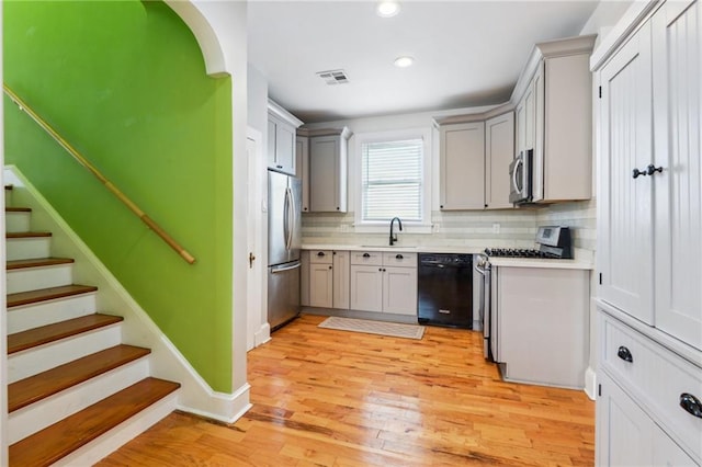 kitchen with gray cabinets, light wood-type flooring, tasteful backsplash, sink, and appliances with stainless steel finishes