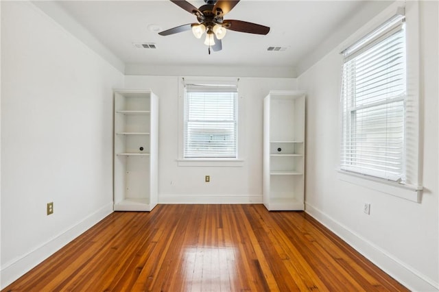 empty room with wood-type flooring, visible vents, ceiling fan, and baseboards