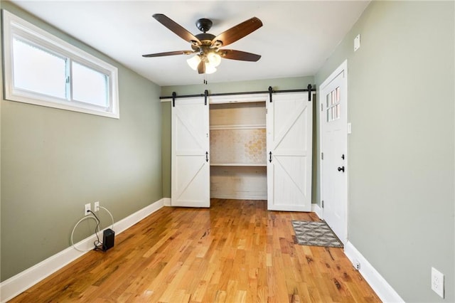 unfurnished bedroom with baseboards, a barn door, ceiling fan, and light wood-style floors