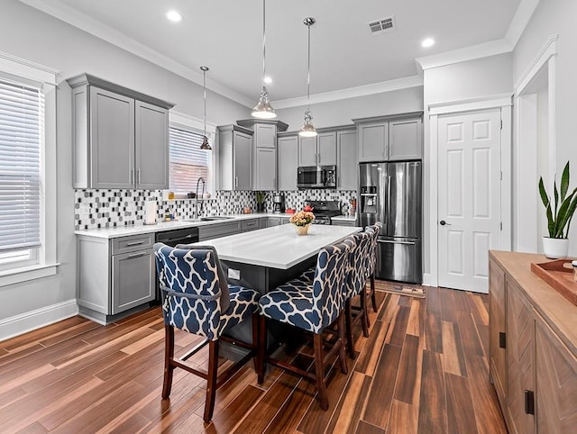 kitchen featuring appliances with stainless steel finishes, dark wood-type flooring, pendant lighting, a kitchen bar, and sink