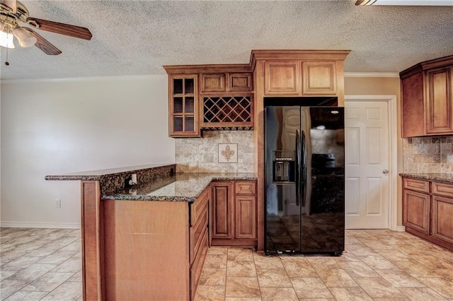 kitchen featuring ceiling fan, tasteful backsplash, black fridge with ice dispenser, dark stone countertops, and crown molding