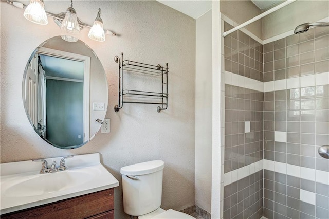 bathroom with tiled shower, vanity, and toilet