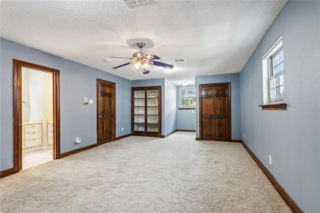 unfurnished bedroom with a textured ceiling, connected bathroom, light colored carpet, and ceiling fan