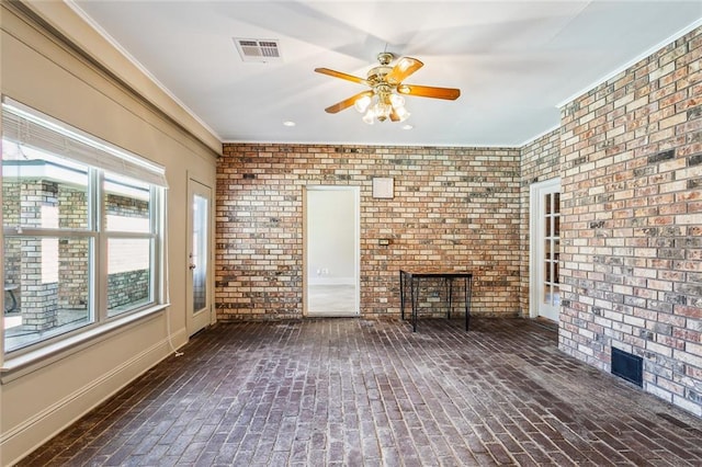 unfurnished living room featuring ceiling fan, crown molding, and brick wall