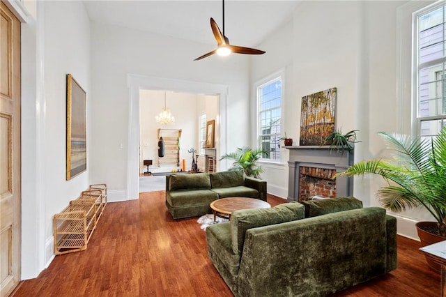 living room with a brick fireplace, hardwood / wood-style flooring, ceiling fan with notable chandelier, and high vaulted ceiling