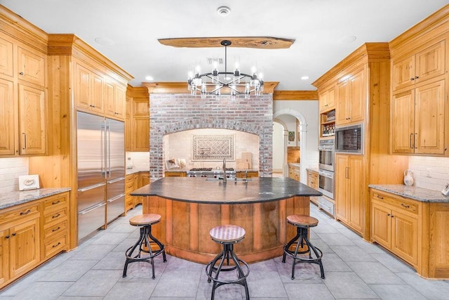 kitchen with pendant lighting, built in appliances, a kitchen breakfast bar, and an island with sink