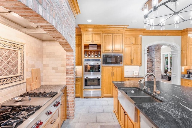 kitchen with sink, light tile patterned floors, appliances with stainless steel finishes, dark stone countertops, and tasteful backsplash