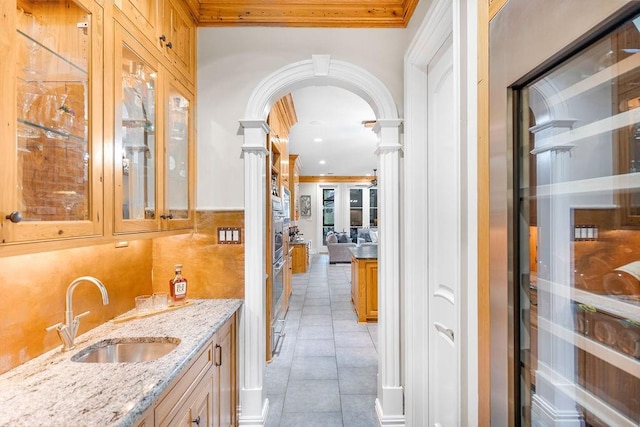 interior space with sink, light tile patterned floors, light stone counters, ornamental molding, and ornate columns