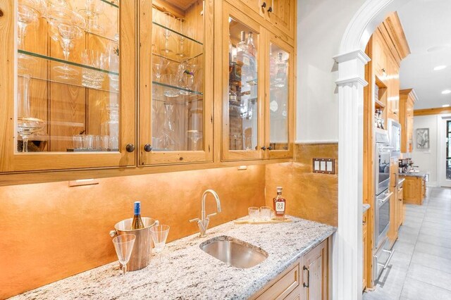 bar featuring decorative columns, sink, light tile patterned floors, light stone counters, and crown molding