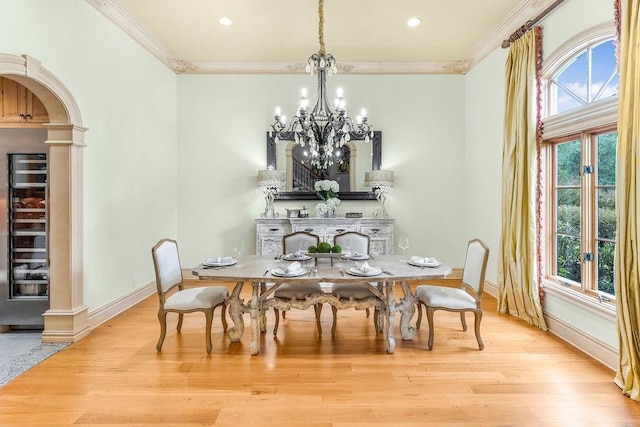 dining area featuring a notable chandelier, ornamental molding, decorative columns, and light wood-type flooring