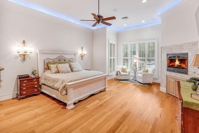 bedroom with a tiled fireplace, ornamental molding, ceiling fan, and light wood-type flooring