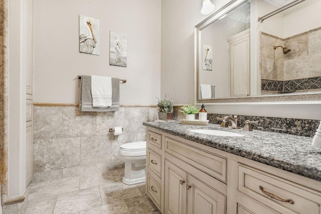 bathroom with vanity, toilet, tile walls, and a tile shower