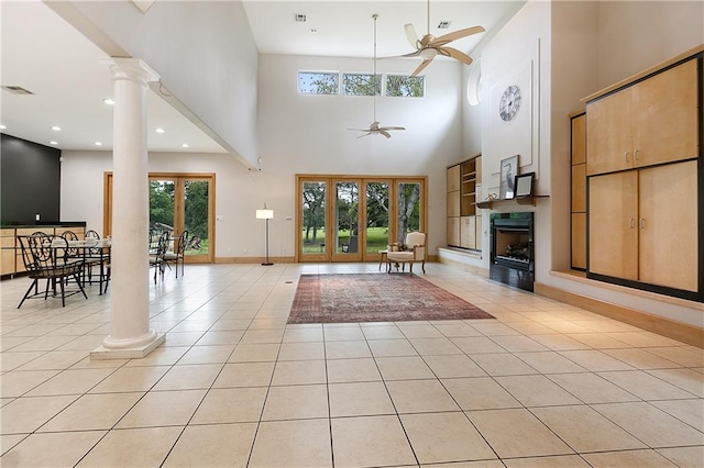 tiled living room with a towering ceiling, ceiling fan, and decorative columns