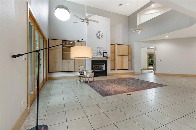 unfurnished living room with ceiling fan, light tile patterned floors, and a high ceiling