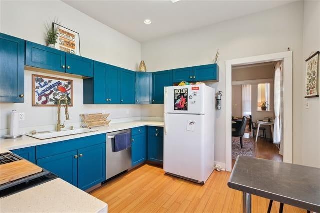 kitchen featuring blue cabinetry, dishwasher, light hardwood / wood-style floors, sink, and white refrigerator