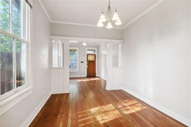 unfurnished dining area with decorative columns, a notable chandelier, wood-type flooring, and crown molding