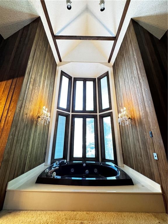 bathroom with wooden walls, vaulted ceiling, a textured ceiling, and a bathtub