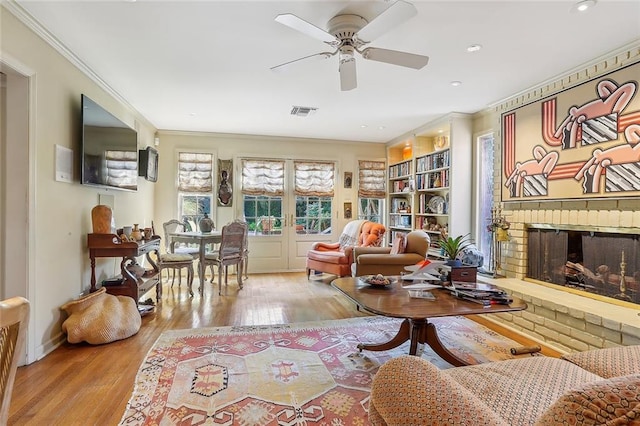 living room featuring ornamental molding, a brick fireplace, light hardwood / wood-style floors, and ceiling fan