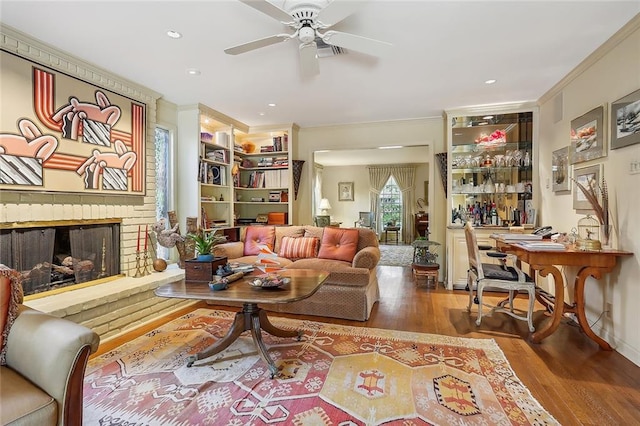 living room with wood-type flooring, a fireplace, crown molding, and ceiling fan