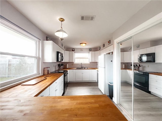 kitchen with black appliances, hanging light fixtures, white cabinets, and wooden counters