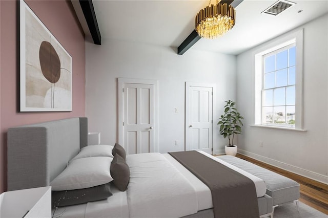 bedroom featuring a notable chandelier, hardwood / wood-style flooring, multiple closets, and beamed ceiling