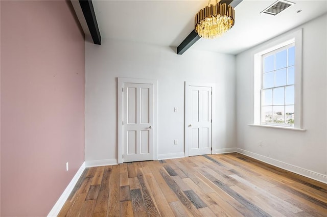 unfurnished bedroom with a notable chandelier, beam ceiling, and light hardwood / wood-style flooring