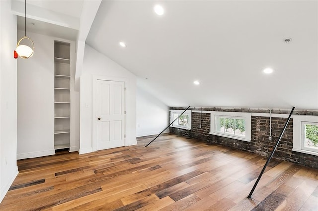 additional living space featuring hardwood / wood-style flooring, brick wall, built in shelves, and vaulted ceiling