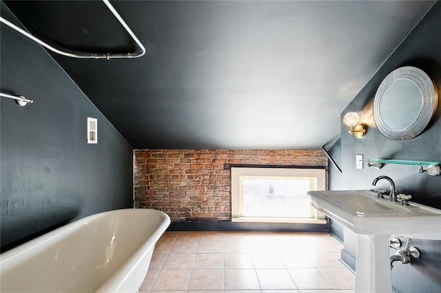 bathroom with brick wall, a tub to relax in, vaulted ceiling, and tile patterned floors