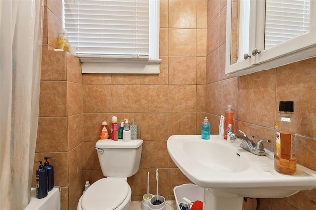 full bathroom featuring tile walls, toilet, shower / bath combo with shower curtain, and sink