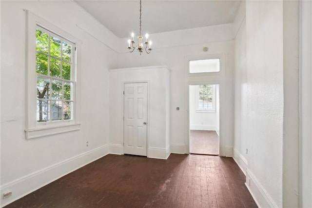 spare room featuring a notable chandelier, dark hardwood / wood-style flooring, and a wealth of natural light